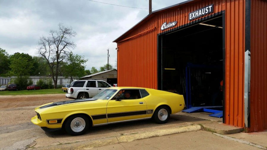 Yellow classic Ford Mustang fastback outside JR Discount Muffler’s custom exhaust shop bay